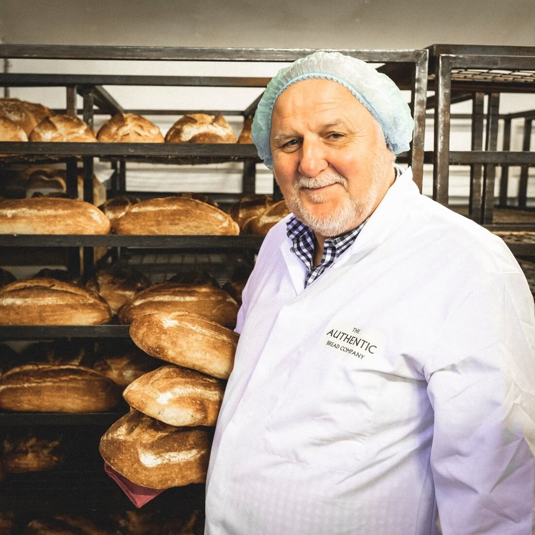 Alan Davis standing beside a rack of freshly baked bread in his bakery,